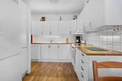 Kjøkken med hvite slette fronter. Fliser over benk. Enkelt å holde rent og pent.