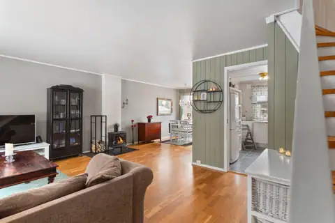 Innholdsrik bolig. Her ser du stue og spisestue med gjennomgående belysning, vedovn, utgang terrasse og hage. Til høyre ser du kjøkkenet.