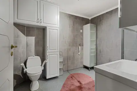 Romslig bad med gode oppbevaringsmuligheter og opplegg for vaskemaskin. Badet har våtromsplater på veggene og belegg på gulvet.
